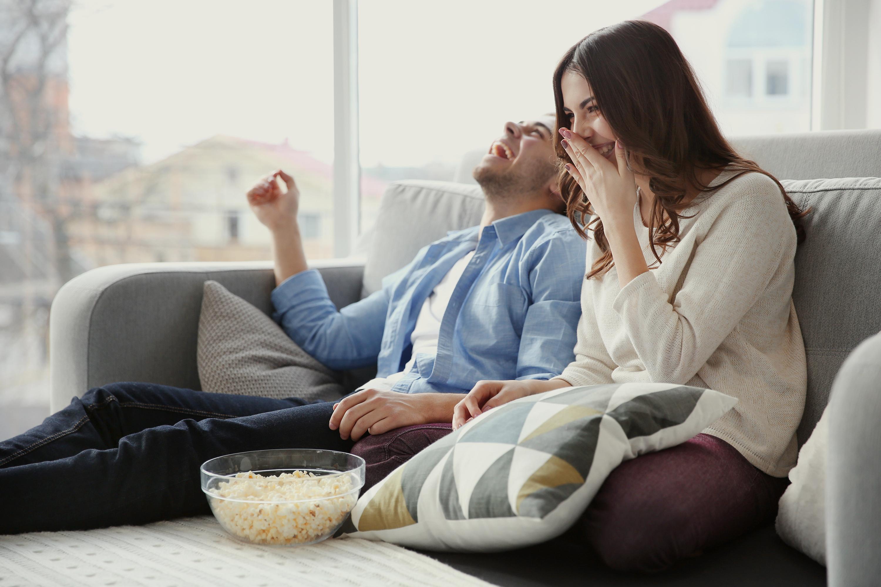 Couple watching TV on sofa in living room while having a snack